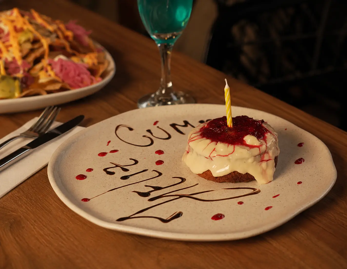 Postre de cumpleaños decorado con crema, salsa de frutos rojos y vela encendida en restaurante Azotea